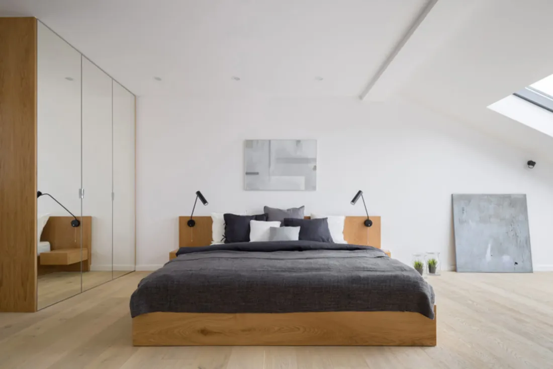 Sypialnia na poddaszu z szafą do sufitu z lustrzanymi drzwiami i łóżkiem na drewnianej ramie